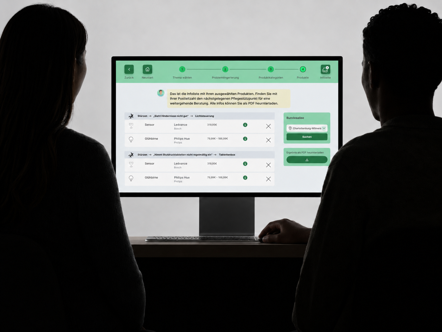 Two people reviewing their assistive-tech shortlist on a monitor, with the care-support finder near the last step